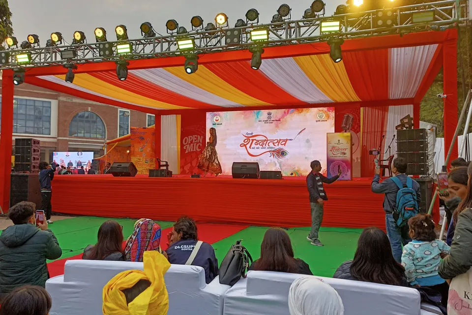 Wide view of the main stage under a red-and-saffron canopy with the audience seated