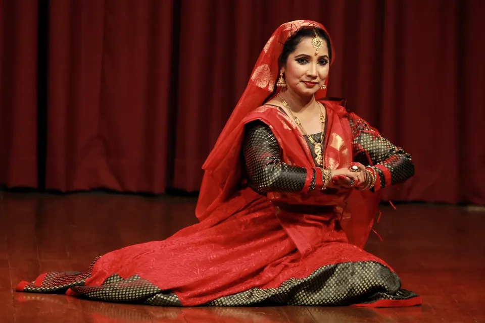 A Kathak dancer in red, seated pose