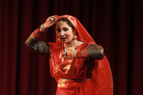 A Kathak dancer in red adjusting her veil
